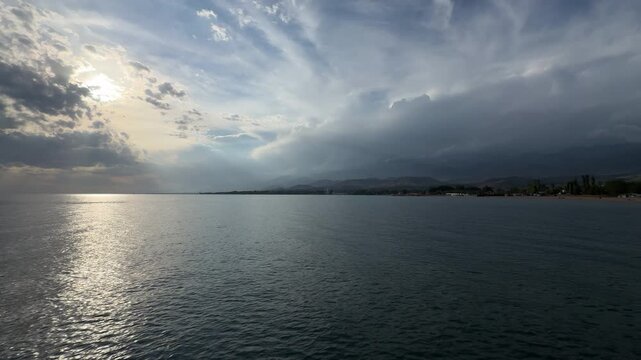 Panoramic view of Lake Issyk-Kul before storm with sun glitter on water and dark thunderclouds in Kyrgyzstan