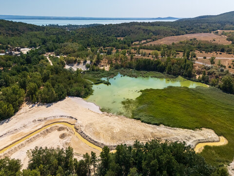 Aerial view of Burnout Lake near Salfold in Hungary's Balaton Uplands, a former quarry lake with forested shoreline, reeds and summer greenery in a protected rural landscape.