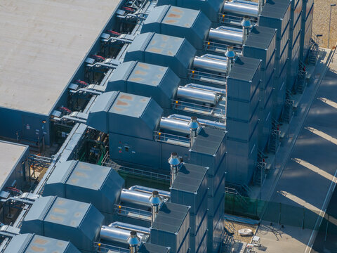 Aerial view of a modern datacenter featuring large industrial cooling units and complex metal piping infrastructure in The Netherlands.