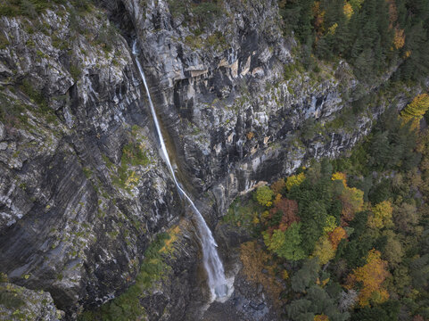 Aerial view of a waterfall cascading down a rocky cliff face in the Pyrenees surrounded by autumn foliage in Spain.