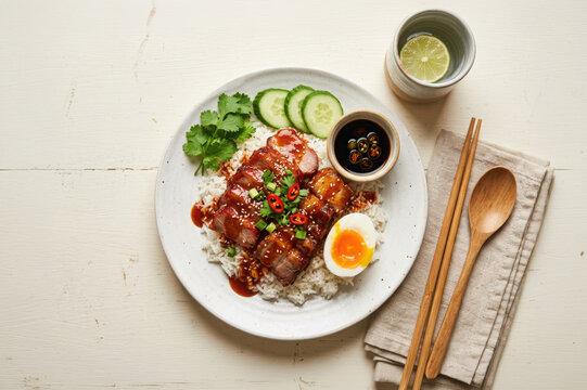 Plate of roasted pork rice topped with soy sauce glaze and sliced boiled egg with cucumber garnish