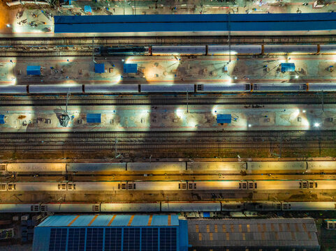 Aerial view of a train station at night with illuminated platforms and parked trains along the tracks in Udaipur, Rajasthan, India.