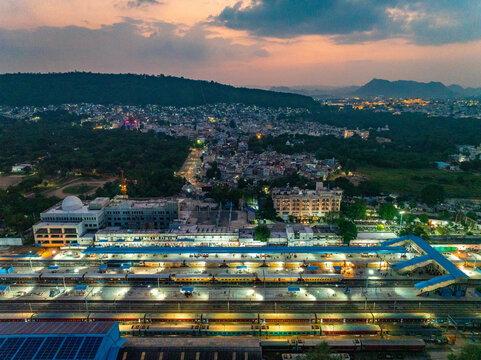 Aerial view of Udaipur Railway Station with trains at the platforms, city lights, and hills in the background at dusk in Udaipur, Rajasthan, India.