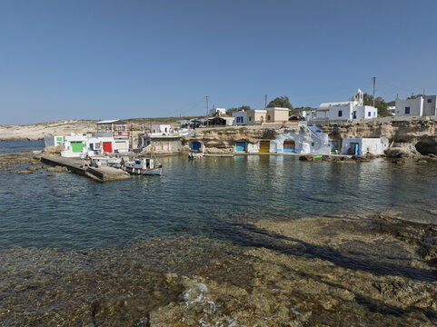 Aerial view of the traditional colorful boat houses known as syrmata carved into the volcanic rock along the turquoise coastline of Milos, Greece.