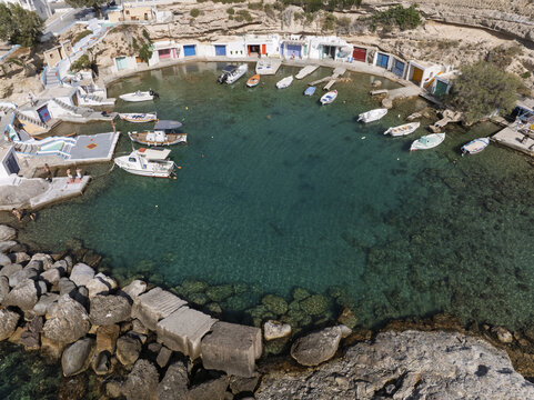 Aerial view of the picturesque fishing village of Klima with colorful boat garages, small fishing boats floating in the turquoise bay, and rocky coastline in Milos, Greece.