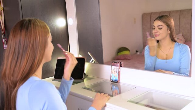 Young beauty blogger creating social media video content while applying makeup with a gua sha stone and recording a tutorial on her smartphone for her online audience