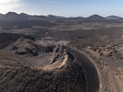 Aerial view of the volcanic landscape of Timanfaya National Park with rugged lava fields, craters, and arid terrain under a clear sky in Lanzarote, Canarias, Spain.