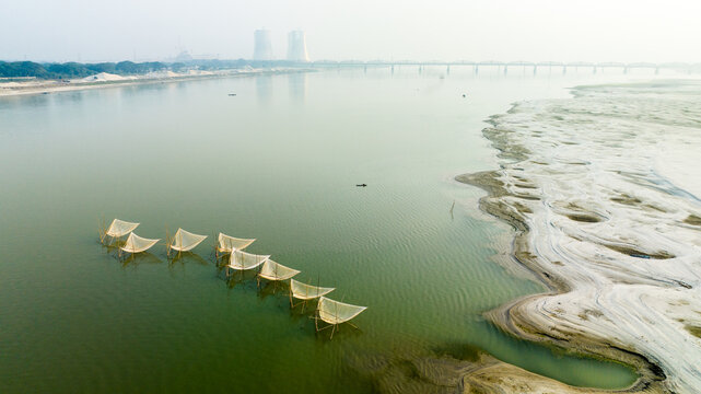 Aerial view of traditional fishing nets set in the Padma River with the Hardinge Bridge and power plant cooling towers in the distance in Pabna, Rajshahi Division, Bangladesh.