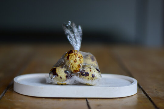 Fresh speckled quail eggs packed in a transparent plastic bag placed on a white oval tray on a wooden surface, concept of grocery shopping and food packaging