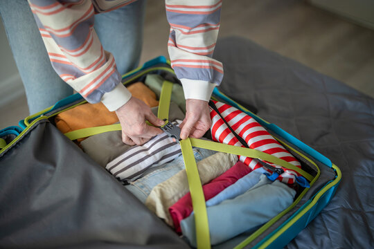 Woman finishing packing suitcase for vacation travel and fastening buckle on suitcase strap, female traveler hands tightening strap in luggage filled with clothing and personal items, ready for trip.