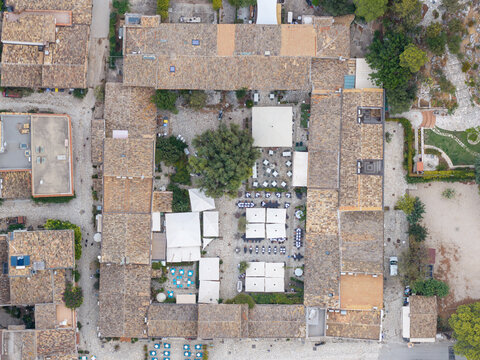 Aerial view of a central courtyard with restaurant tables and umbrellas surrounded by historic stone buildings in San Vito Lo Capo, Sicilia, Italy.