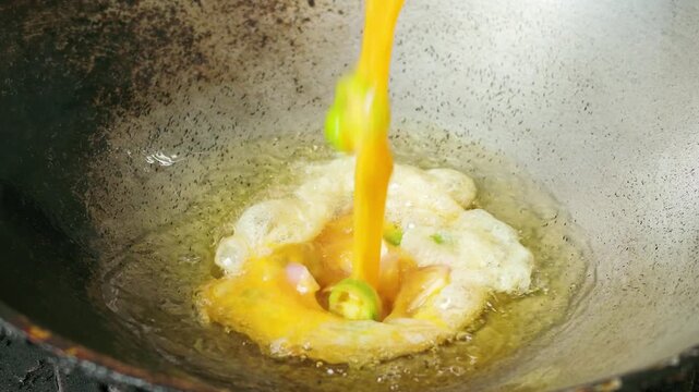 Slow Motion Close-up of Pouring Beaten Egg into Sizzling Hot Oil in Wok