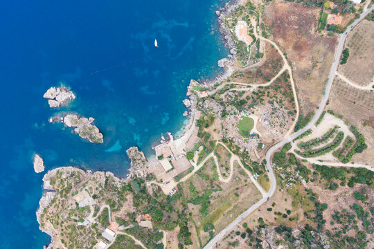Aerial view of Riserva Naturale Orientata dello Zingaro featuring rugged coastal cliffs, turquoise waters, winding roads, and lush vegetation in San Vito Lo Capo, Sicilia, Italy.