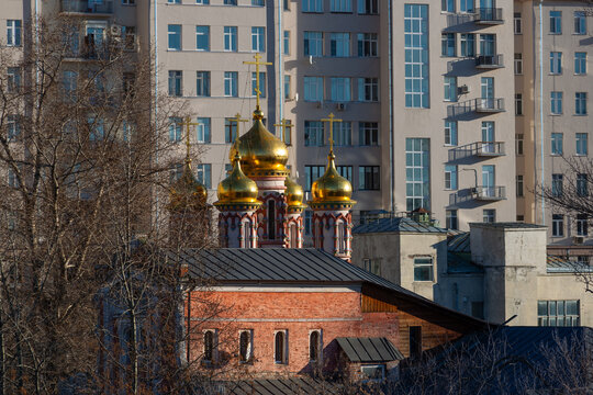Domes and crosses of an Orthodox church set against the backdrop of a residential building in Moscow, the capital of Russia.