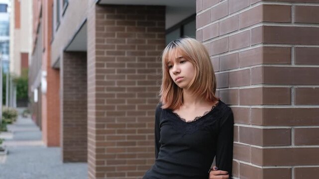 Teen girl facing the camera near a brick building, showing guarded confidence and emotional self control