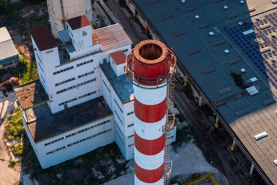 Aerial view of an industrial facility featuring a prominent red and white striped chimney, a large white building, and a warehouse with solar panels in Nera Montoro, Umbria, Italy.