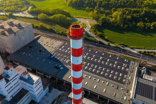 Aerial view of an industrial facility featuring a prominent red and white striped chimney and extensive solar panels on the roof, situated near railway tracks in Nera Montoro, Umbria, Italy.