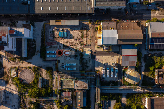 Aerial view of an industrial facility featuring a tall chimney, storage tanks, and various factory buildings with long shadows cast across the site in Nera Montoro, Umbria, Italy.