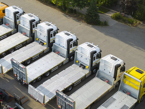 Aerial view of a row of white flatbed trucks parked in an orderly line on a paved lot in Krakow, Lesser Poland Voivode, Poland.