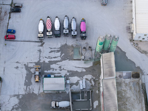 Aerial view of a concrete plant featuring a row of parked cement mixer trucks, industrial silos, and storage facilities in Krakow, Lesser Poland Voivode, Poland.
