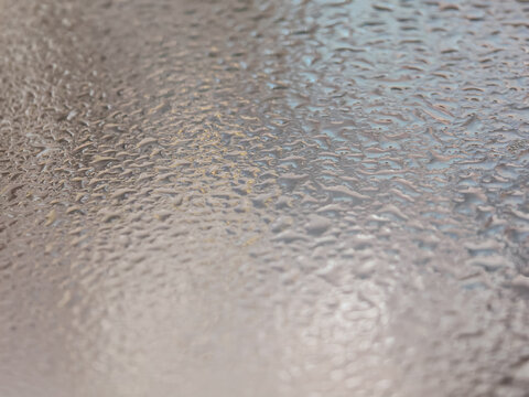 Extreme macro photography of clear water droplets and condensation forming on a smooth metallic surface. Features a shallow depth of field with soft bokeh, highlighting the natural liquid details