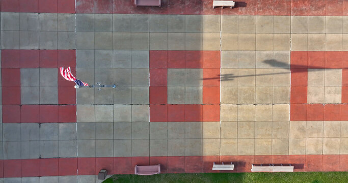 Aerial view of a paved square with a red and grey geometric pattern, featuring a flagpole with an American flag and benches in Elizabethtown, Pennsylvania, United States.