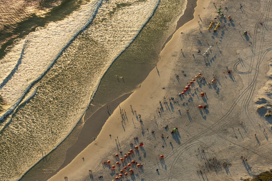 Aerial view of a sandy beach with colorful umbrellas, people walking and relaxing on the sand, and gentle waves rolling onto the shore in Rio de Janeiro, Rio de Janeiro, Brazil.