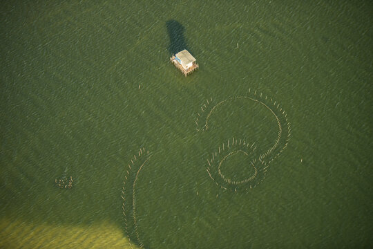 Aerial view of a small stilt house and circular fishing stakes in the calm green waters of the bay in Rio de Janeiro, Rio de Janeiro, Brazil.