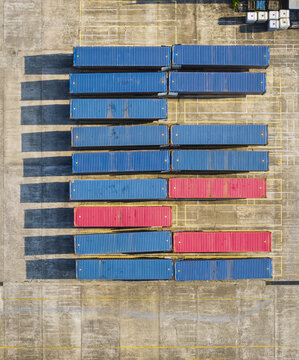 Aerial view of rows of blue and red shipping containers neatly arranged in a logistics yard with long shadows cast on the concrete ground in Taiwan.
