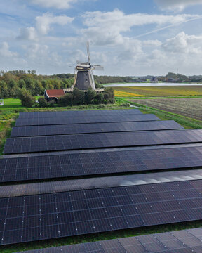 Aerial view of Molen De Hoop windmill situated next to a large solar panel farm in the rural landscape of 't Zand, North Holland, Netherlands.