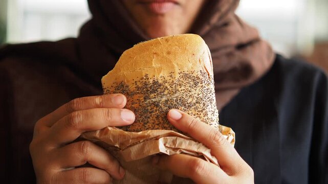 Woman holds a sandwich wrapped in paper while staring at it in a cafe