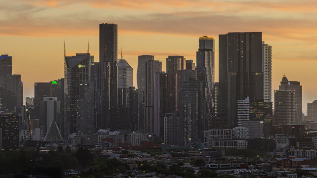 Aerial view of the Melbourne CBD skyline featuring modern skyscrapers and glass towers illuminated by the warm glow of a sunset in Melbourne, Victoria, Australia.