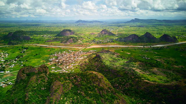 Aerial view of the rocky hills of Dass surrounded by lush green fields, a winding river, and rural settlements in the landscape of Bauchi, Bauchi, Nigeria.