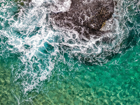 Aerial view of Cudgen Headland South Head with turquoise ocean water and white sea foam crashing against dark rocks in Kingscliff, New South Wales, Australia.