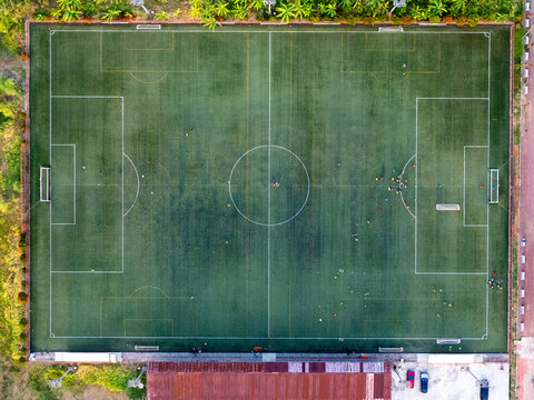 Aerial view of a soccer field with players on the green turf, white markings, and surrounding vegetation in Cilacap, Central Java, Indonesia.
