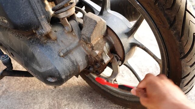 Man Cleaning Motorcycle Rear Wheel and Brake Caliper with Brush During Maintenance
