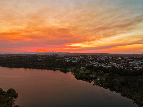 Aerial view of the coastal town of Kingscliff at sunset with vibrant orange clouds reflecting over the river and surrounding landscape in Kingscliff, New South Wales, Australia.
