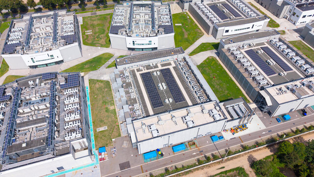Aerial view of a modern data center campus with large industrial buildings, solar panels, and HVAC units on flat roofs, surrounded by green lawns in Milan, Lombardy, Italy.