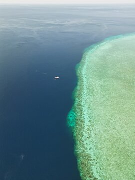 Aerial view of Pulau Ndaa coral reef with a small boat floating in the deep blue sea, Tomia, South East Sulawesi, Indonesia.