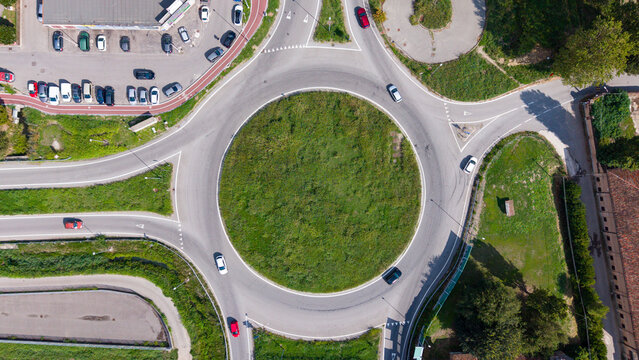 Aerial view of a roundabout with cars driving on the asphalt road and a green grassy center surrounded by parking spaces and trees in Milan, Lombardy, Italy.