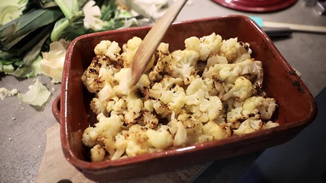 Stockholm, Sweden A cook mixes grilled cauliflower florets with a wooden utensil in an earthenware dish.