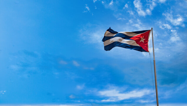 Cuban national flag waving against a bright blue sky with scattered clouds