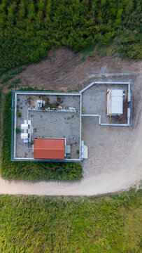 Aerial view of a gas substation with a red roof building and fenced enclosure surrounded by green fields in San Giuliano Milanese, Lombardy, Italy.