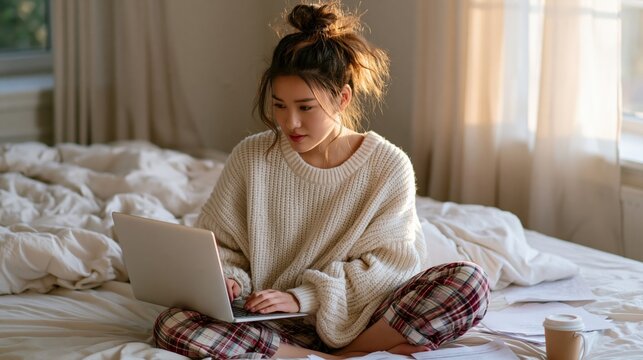 Young woman working on laptop in bed, enjoying comfort and productivity in morning light