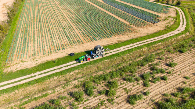 Aerial view of a tractor pulling a reel irrigation system across a cultivated agricultural field in Bettola-Zeloforomagno, Lombardy, Italy.