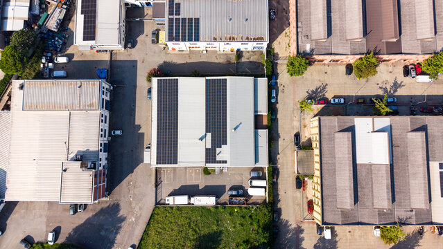 Aerial view of an industrial zone featuring warehouses with solar panels on rooftops, parking areas, and surrounding roads in Milan, Lombardy, Italy.