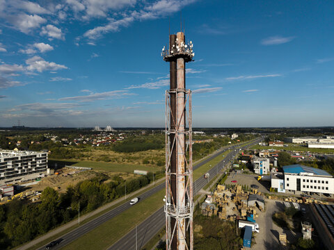 Aerial view of a tall industrial chimney equipped with communication antennas, rising above a highway and surrounding urban landscape in Krakow, Lesser Poland Voivode, Poland.