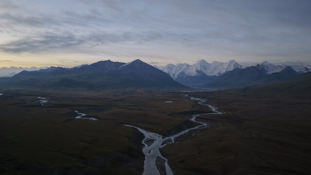 Aerial view of the Engilchek Glacier surrounded by winding rivers and rugged mountain peaks under a twilight sky in Ak-Su, Issyk-Kul Region, Kyrgyzstan.