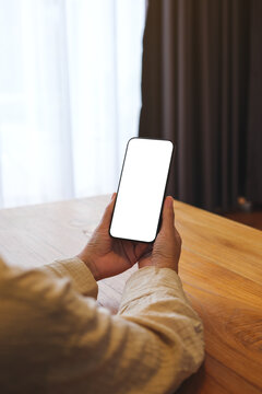 Vertical mockup image of a woman holding and using mobile phone with blank desktop white screen at home