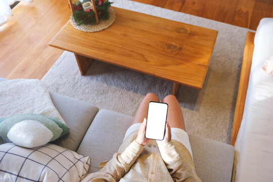 Top view mockup image of a woman holding and using mobile phone with blank desktop white screen at home